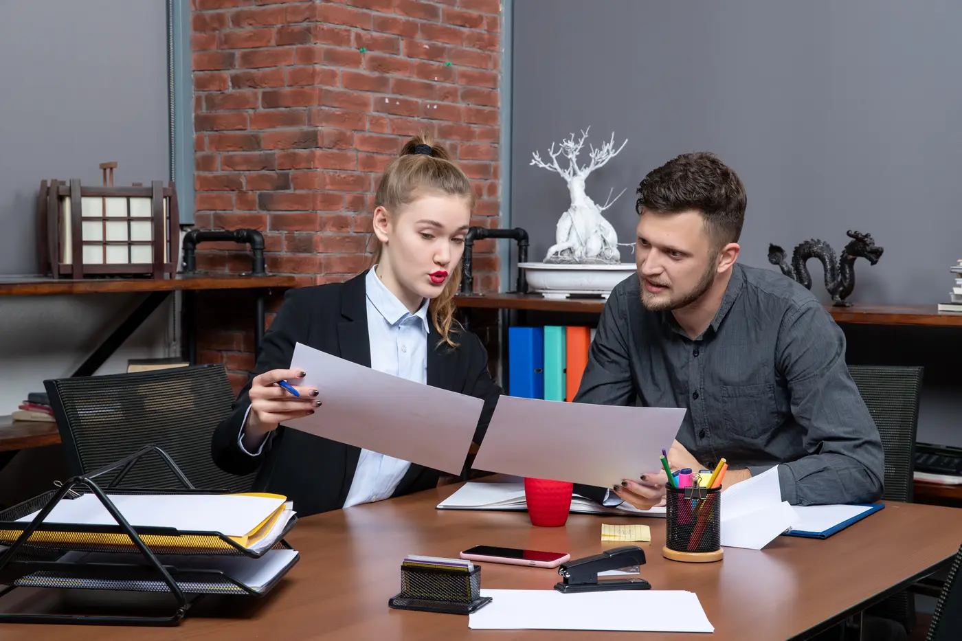 Escena de reunión en una sala corporativa: una carpeta sobre la mesa y dos profesionales comparando documentos